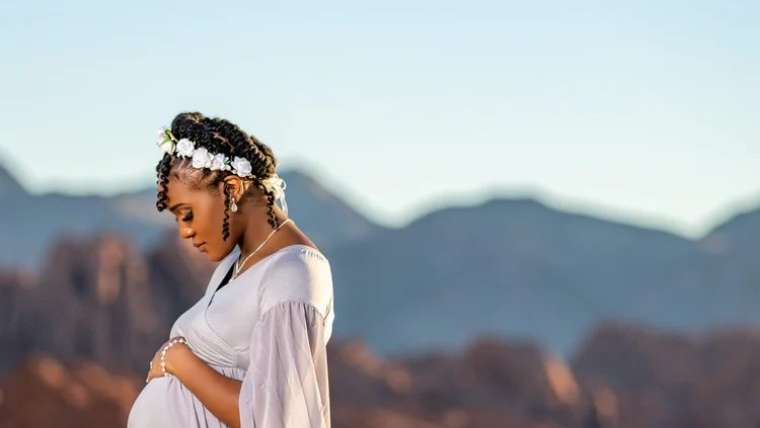 Expecting mother in a cream gown on a desert ridge at sunset, Las Vegas maternity photography